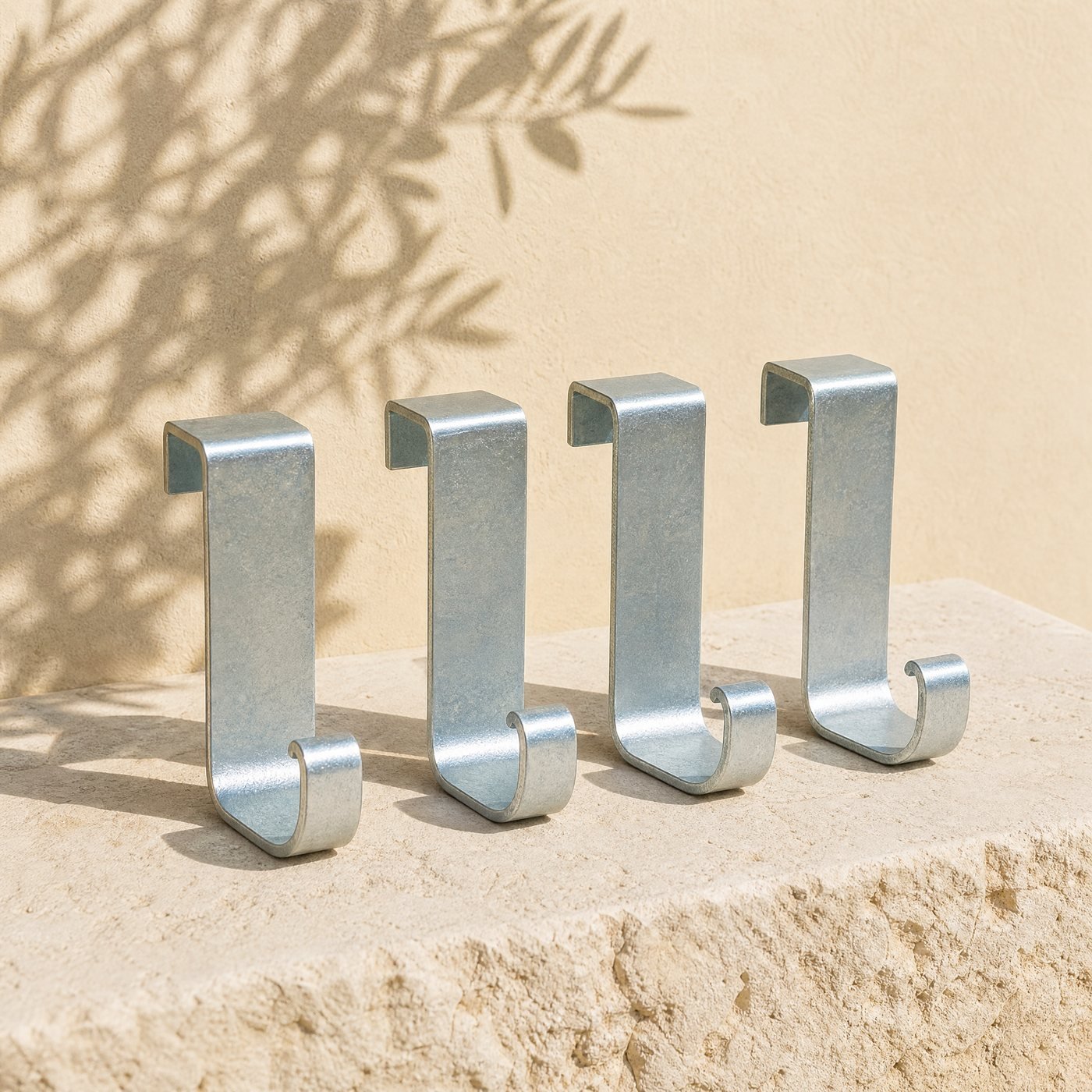 Over-fence Hooks, Set of 4 — four zinc-plated steel over-fence hooks with a flat bend and a curled hook end, laid in a row on sunlit stone