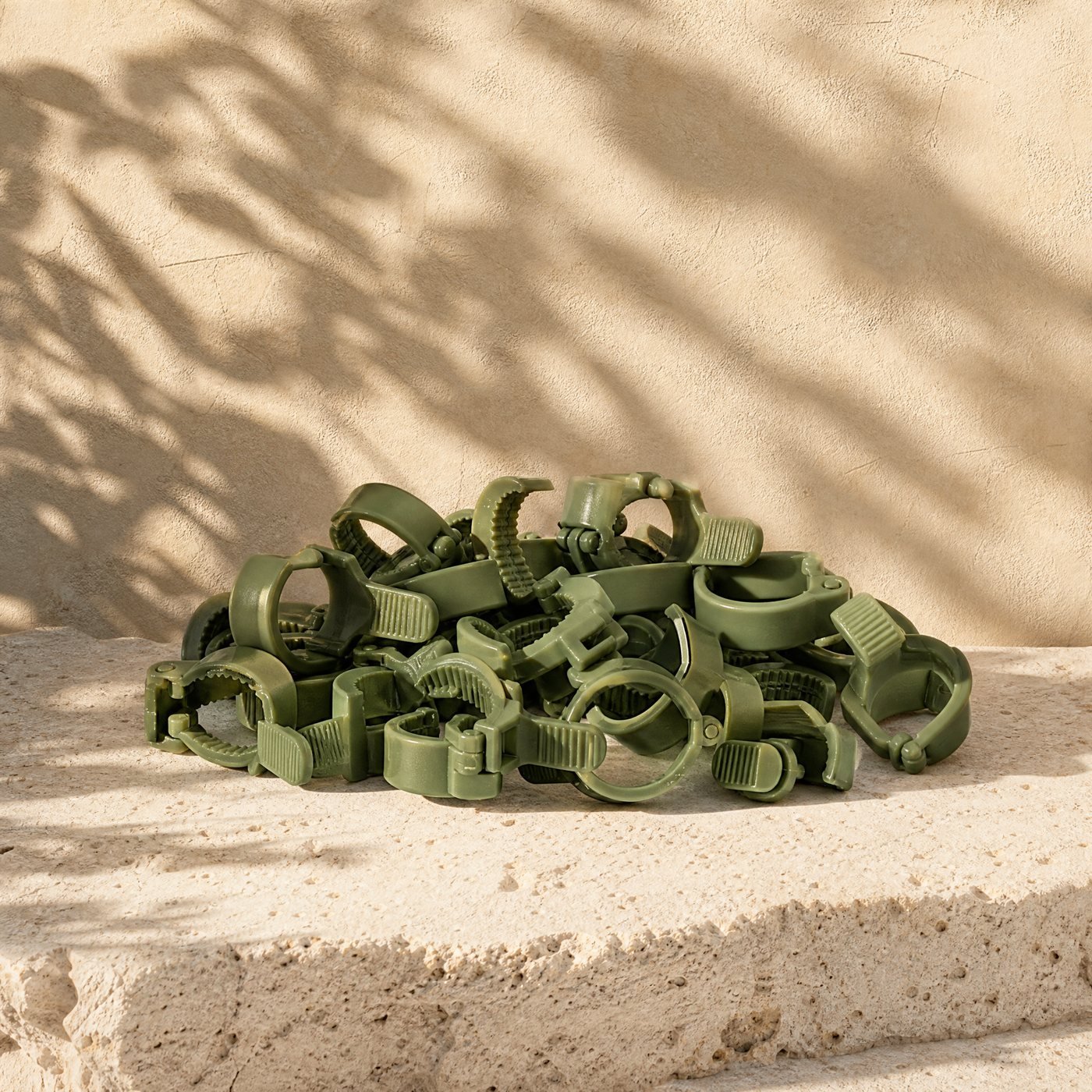 Plant Support Clips, Pack of 50 — a small heap of green hinged nylon plant support clips on sunlit stone