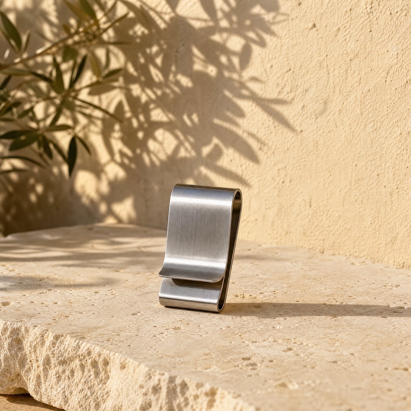 Glove & Tool Clip — a small stainless steel spring belt clip holding nothing, lying on a sunlit stone slab