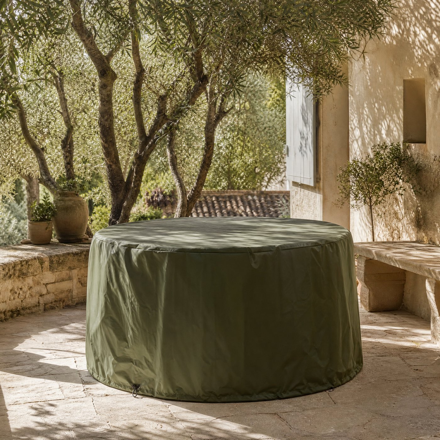 Round Patio Set Cover — a stone terrace with this round cover over a garden table set, trees behind