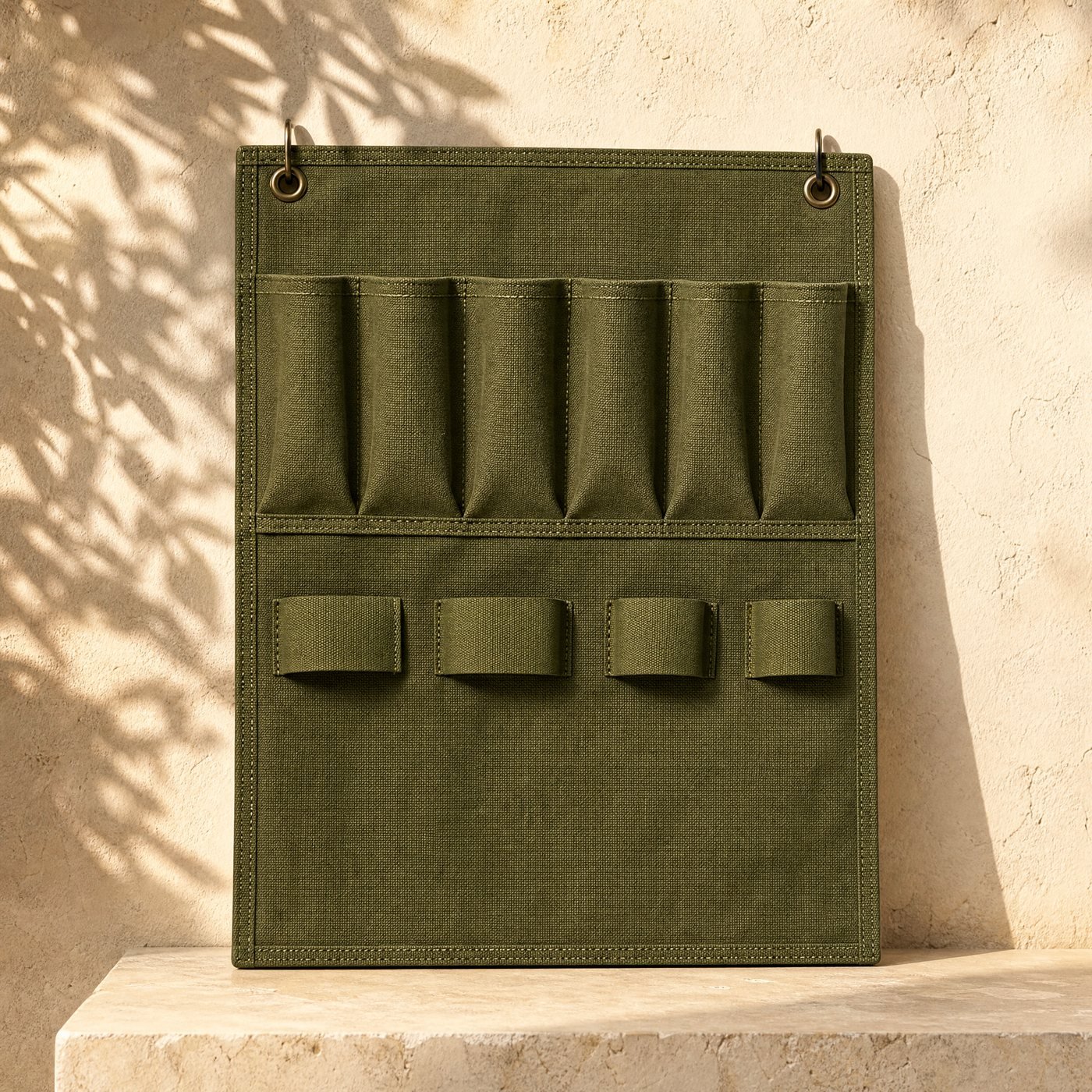 Hanging Tool Organiser — a wall-hung olive-green polyester tool organiser panel with six pockets and four loops, empty, hanging from two eyelets