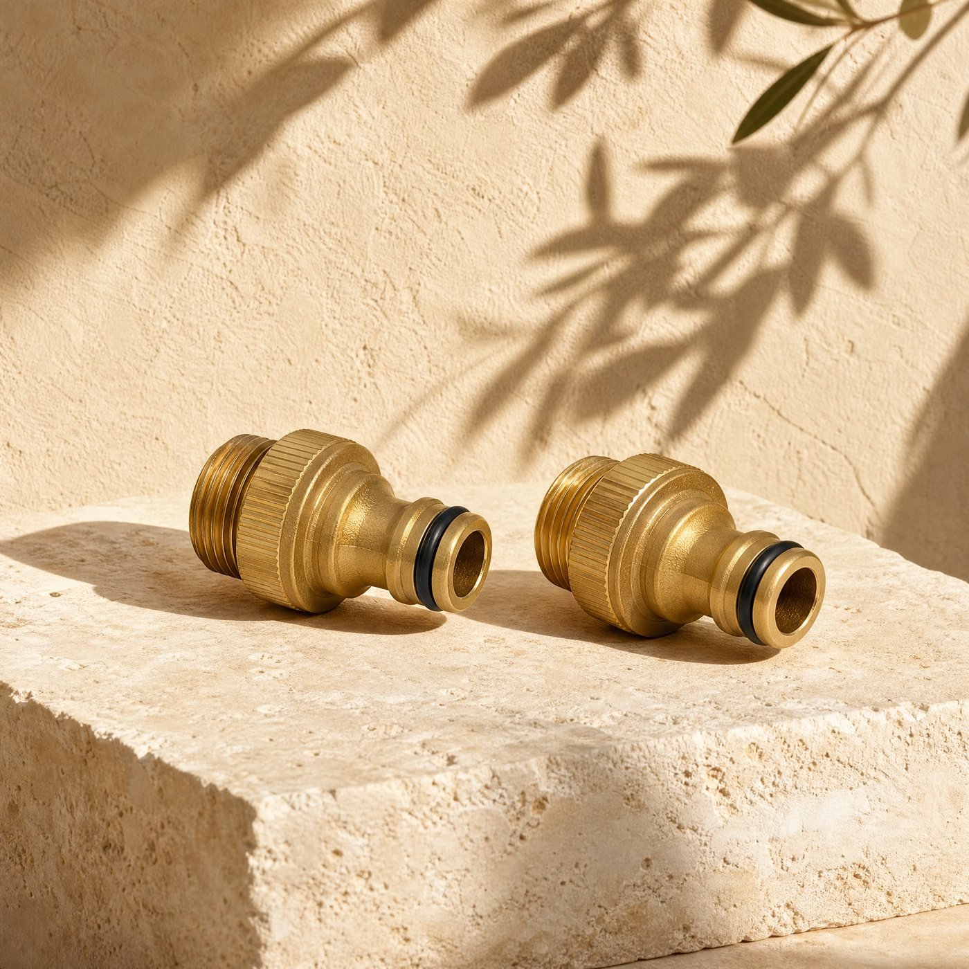Tap Connector Set, G1/2 & G3/4 — two brass-tone plastic garden tap connectors with threaded ends and click-on nozzles, lying on sunlit stone